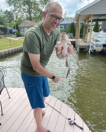Steffen Maier on a dock, holding a catfish he has just caught.